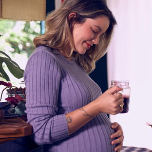 Image of a pregnant woman, wearing a purple blouse and holding a mug with juice.