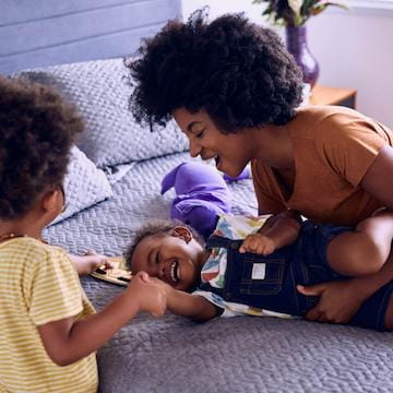 Nubank Life: picture of a mom playing with her baby child and her daughter on a bed.