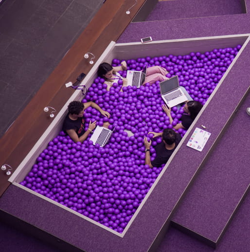 Topshot of four people inside Nubank's purple ball pool with their laptops