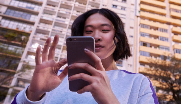 Imagem de uma mulher ao ar livre olhando para a tela do celular enquanto o segura em suas mãos.